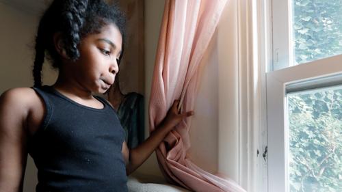 Jasmine Pennington's daughter Nylah Green, 9, pulls a bedroom curtain back revealing mold growing around the window in their Philadelphia rental unit.